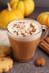 Delicious pumpkin latte in glass cup, spices, cookies and fresh vegetables on grey textured table, closeup