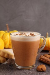 Delicious pumpkin latte in glass cup, spices, cookies and fresh vegetables on grey textured table, closeup