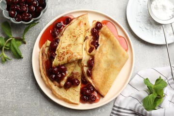 Tasty crepes with cherries, jam and mint served on light table, flat lay