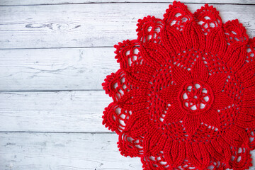 Red crocheted doily placed on a gray wooden background, creating a simple yet elegant handmade textile composition suitable for craft themes, rustic decor, and seasonal creative designs.