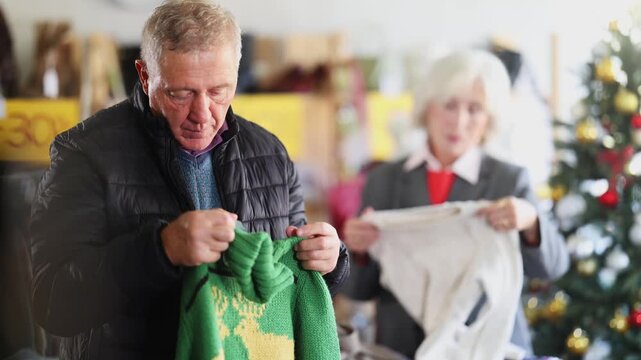 Uncertain old man looking for warm pullover in retail outlet during X-mas sell-out