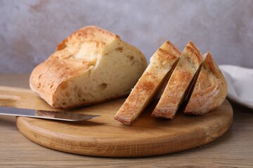 Cut fresh bread and knife on wooden table, closeup
