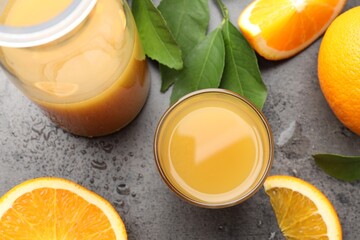 Fresh orange juice, fruits and leaves on grey table, flat lay
