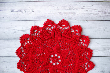 Red crocheted doily placed on a gray wooden background, creating a simple yet elegant handmade textile composition suitable for craft themes, rustic decor, and seasonal creative designs.