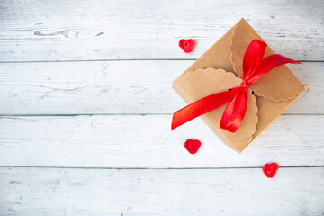 Gift box wrapped with a red ribbon placed on a gray background with small hearts beside it, creating a romantic festive composition perfect for Valentine&rsquo;s Day, love themes and holiday greetings.