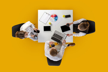 Top view of team collaborating with laptop and charts while drinking coffee. Concept of business planning, marketing workflow, seminar content and corporate routines.