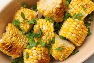 Pieces of grilled corn cobs with green onions on table, closeup