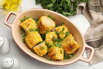 Pieces of grilled corn cobs with green onions on white table, flat lay