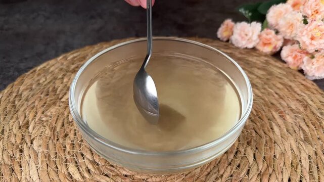 Pouring hot water onto a brown bouillon cube and stirring to dissolve in a glass bowl