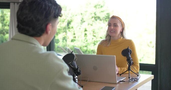 Diverse coworkers initiating handshake across desk with microphones and laptop, preparing podcast
