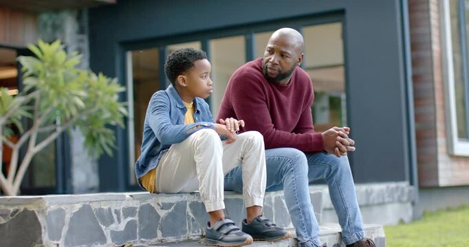African American father and son sitting on steps, he noticing son's fidgeting and offering guidance