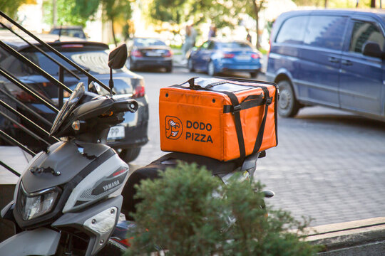 19.11.2025, Batumi, Georgia: Dodo pizza food delivery scooter with branded orange pizza bag parked on urban street with cars, representing fast service, takeaway meals, city logistics,