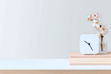 White modern clock on stacked books with delicate orchid blossom in vase creating calm minimalist workspace mood