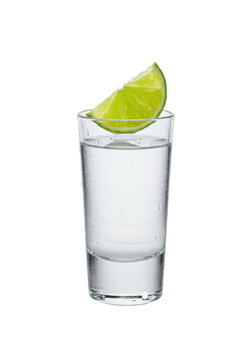 a sweating caballito shot glass filled with crystal clear blanco tequila, centered on a glossy white reflective surface with a transparent background. Emerald lime wedge balanced on the rim,