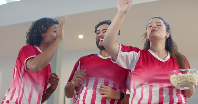 Diverse friends wearing red jerseys cheering win at home highfiving pumping fists grabbing popcorn