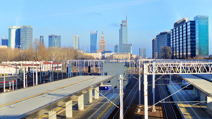 Tracks and electric high voltage for electric trains wires on reinforced concrete and metal masts against the backdrop of a railway station and city skyscrapers on a winter day.