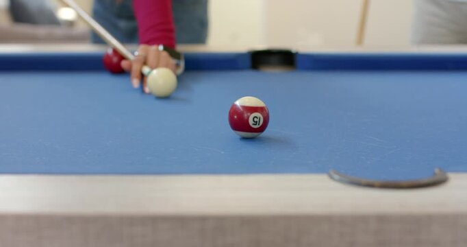After aiming, Woman striking cue ball with cue stick on pool table to pocket striped 15-ball