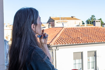 Woman smoking a hand rolled cigarette, looking at urban terracotta rooftops from a balcony