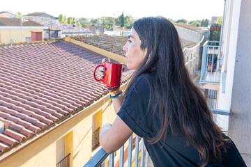 Woman holding a red mug, looking out from a balcony over a town
