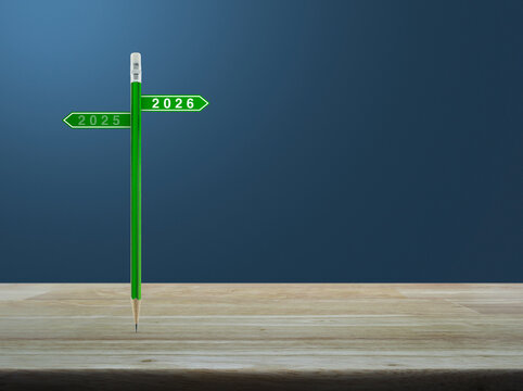 2026 and 2025 direction sign plate with green pencil on wooden table over light blue wall, Business happy new year 2026 planning and strategy concept