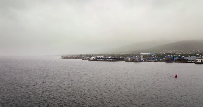 Drone footage over the strait towards Sortland Bridge in Vester&aring;len. A moody, cloudy day in Northern Norway featuring the town coastline, mountains, and calm sea