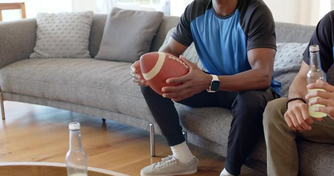 Diverse male friends at home noticing football on coffee table, man rotating ball practicing grip