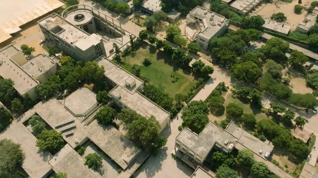 Downward tilted aerial drone footage over NED University of Engineering and Technology campus at noon, showing students walking in the central yard and green areas under intense sun.