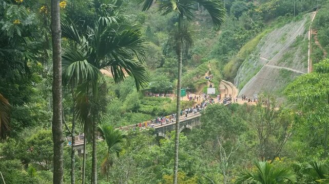 Jungle foliage opens to a view of the Nine Arch Bridge tourist attraction near Ella Sri Lanka where visitors walk along the historic railway span set in lush tropical scenery