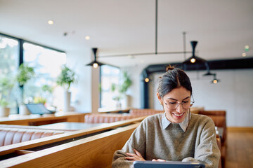 Young woman smiling and using a digital tablet at a modern cafe. Exploring connectivity and flexible remote work lifestyle