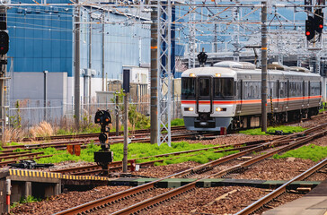 Obraz premium A commuter train on railway tracks in Japan, set against a background of modern city buildings and mountains. Urban travel and public transit concept.