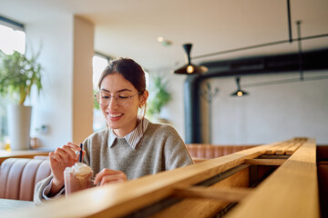 Woman smiling, relaxing and stirring her hot chocolate with whipped cream in a modern, cozy coffee shop