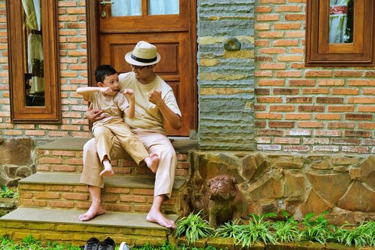 A father and his young son playfully sparring on the stone steps, with the boy pretending to punch while they enjoy a fun bonding moment outdoors.
