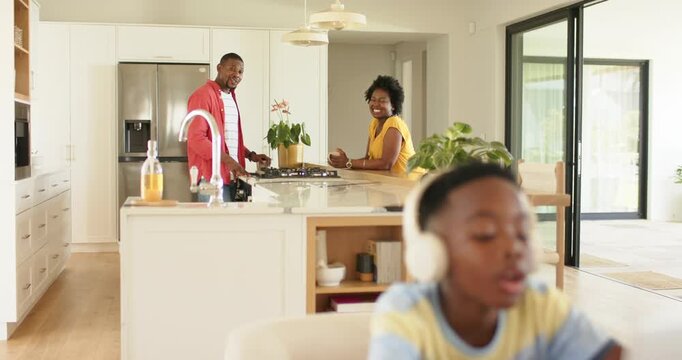 African American boy reacting to camera refocus adjusting headphones typing reply on laptop at home