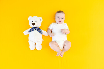 Portrait of cheerful baby boy playing with teddy bear on yellow background