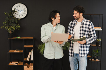 Diverse colleagues collaborating, analyzing data on laptop in modern office space