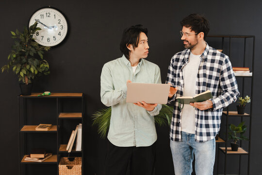 Diverse colleagues collaborating, analyzing data on laptop in modern office space