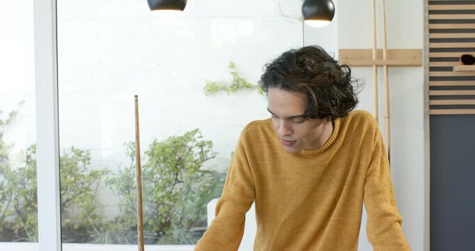 Man leaning on low table inspecting document in modern studio, lifting head and smiling at camera