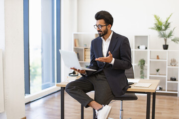 An Indian businessman is using a laptop to have a video call in his office