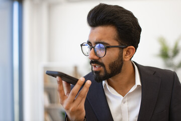 An Indian businessman is speaking into his phone while wearing glasses and a suit jacket