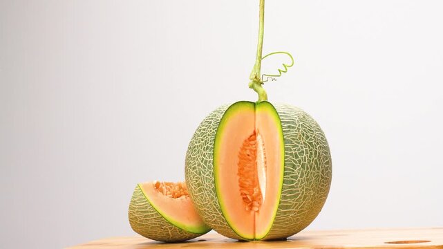 Rotating sliced green netted melon on white background. Fresh orange flesh fruit on wood. Cinematic food concept.
