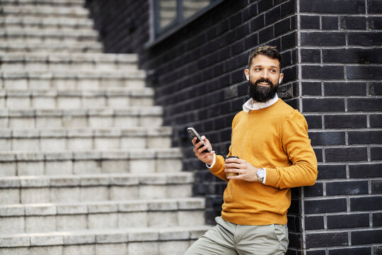 Portrait of business casual man leaning on a wall near stairs on a city street and typing messages on cellphone. - Powered by Adobe