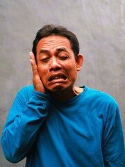 Fototapeta premium An authentic close-up portrait of a Southeast Asian man making a funny, silly, or 'ugly' face, highlighting the concept that happiness is the best medicine for mental health