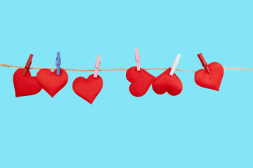 Small red hearts are clipped to a string with colorful clips. The scene features a bright blue background, making it suitable for Valentine's Day designs and digital content.