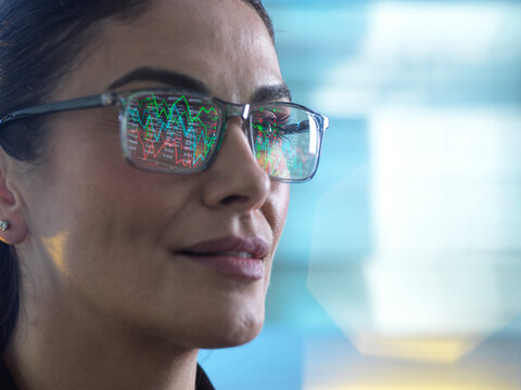 Financial analyst viewing market data on screen with graphs reflecting in glasses