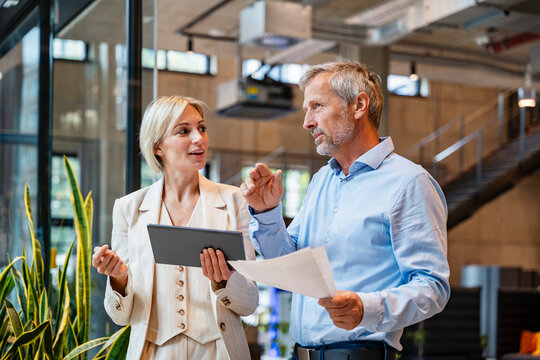 Colleagues discussing business in a modern office holding tablet and papers