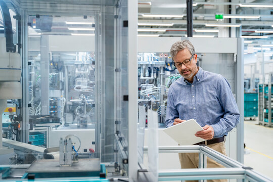 Engineer in industrial automation monitoring machinery with clipboard