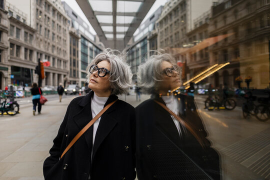 Businesswoman in smart casual looking up with reflection in city street