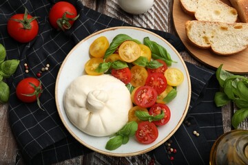 Delicious burrata cheese with basil and tomatoes on wooden table, flat lay