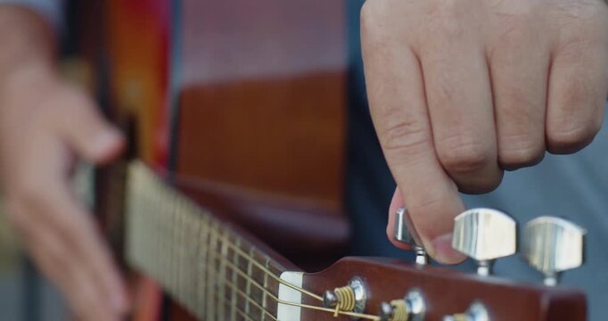 Experience the art of tuning your guitar as our hands carefully adjust the tuning pegs, creating the perfect sound for your music. Slow motion 4k footage.