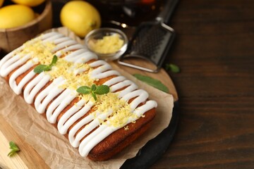 Tasty lemon cake decorated with icing, zest and mint served on wooden table, closeup. Space for text